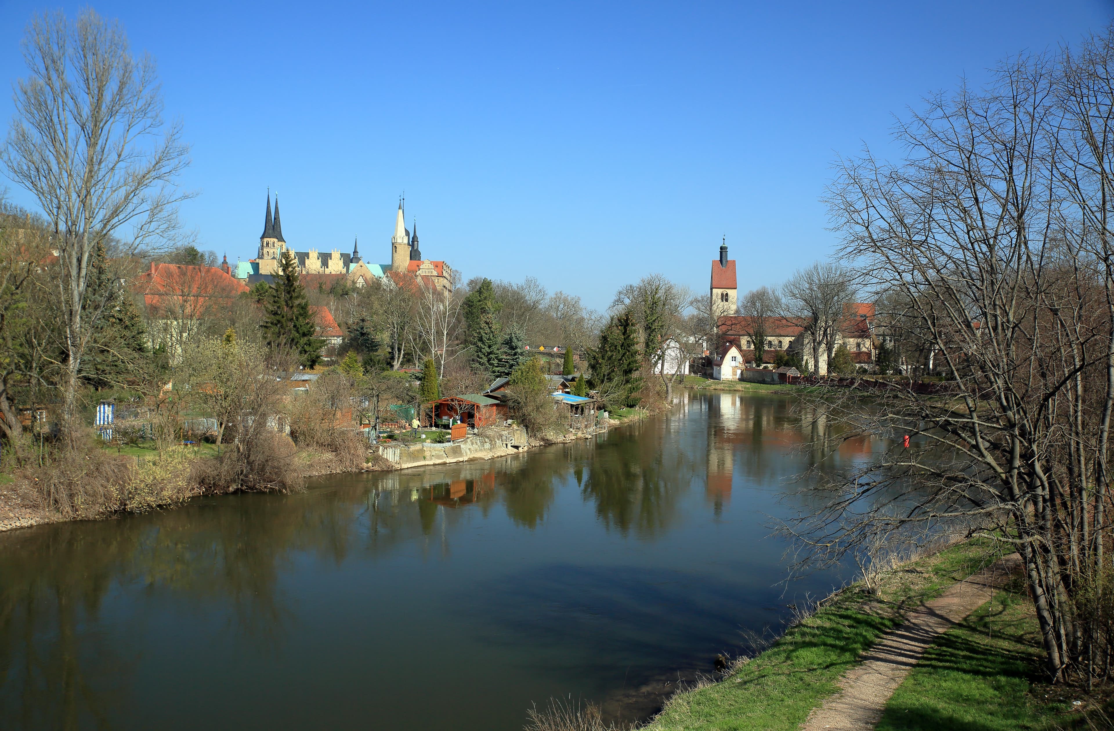 Blick von der Saalebrücke auf die Saale mit Schloss, Dom und Neumarktkirche von Merseburg im Hintergrund, an einem klaren Frühlingstag.